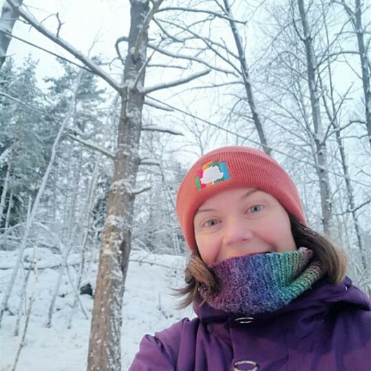 Female team member in beanie in front of snowy trees