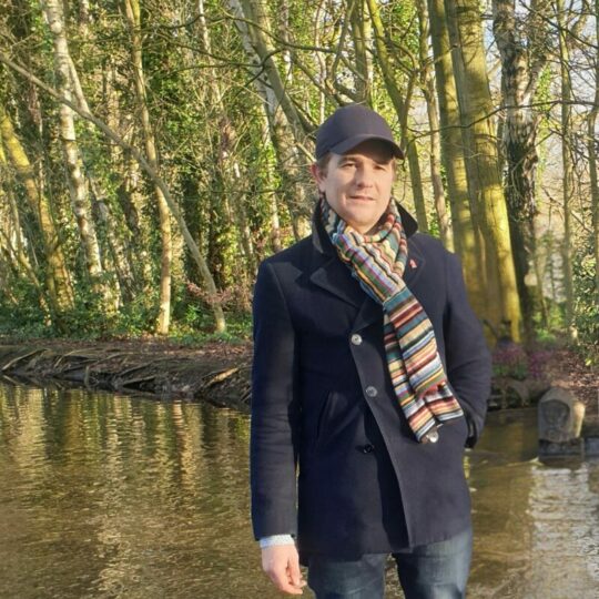 Man in hat and scarf standing in front of trees