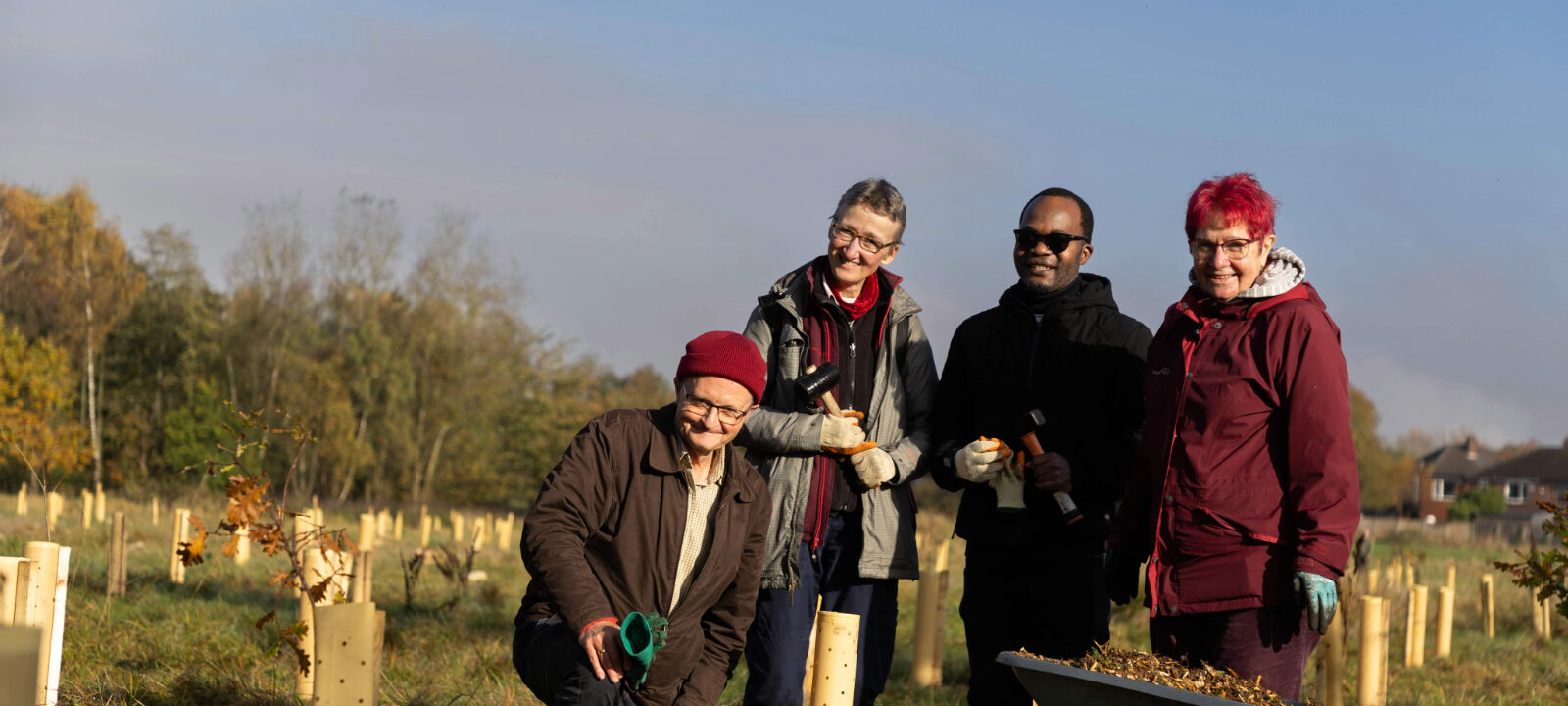 four individuals posing at tree planting event, smiling towards camera