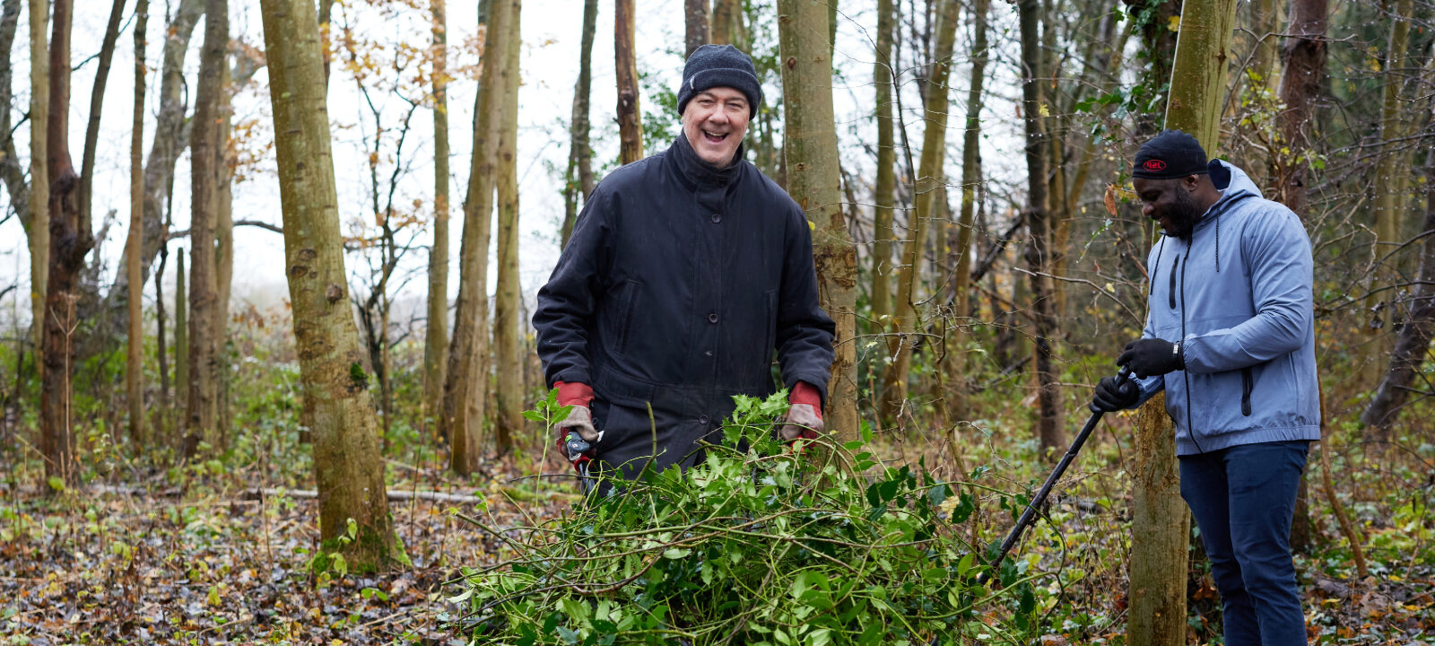 two men taking part in woodland management with a wheel barrow